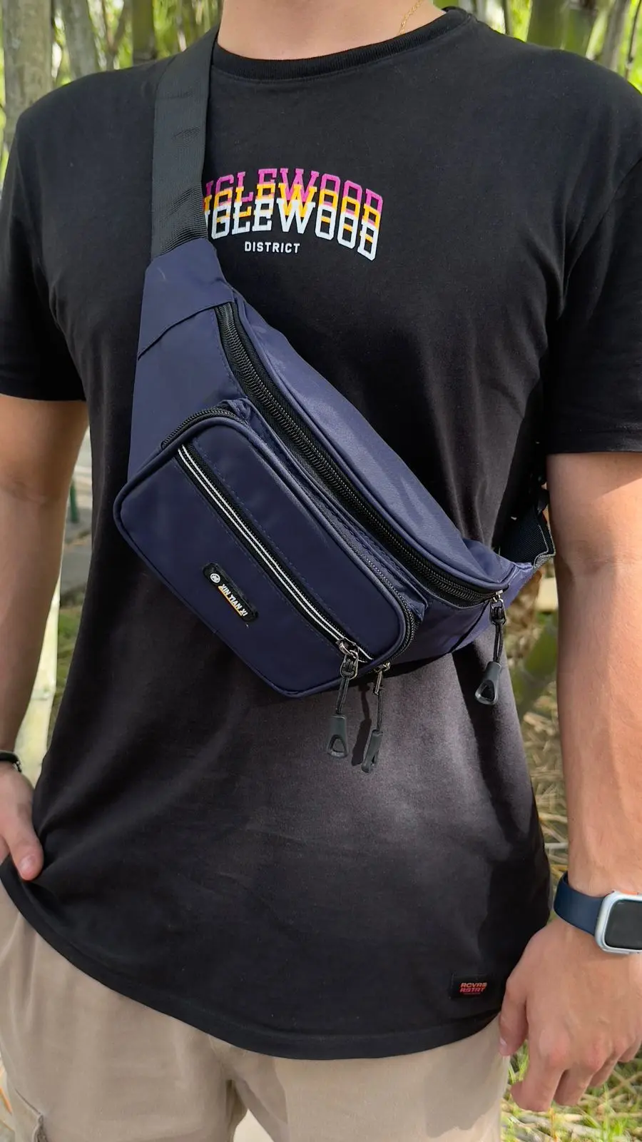 Riñonera azul oscuro de hombre con correa ajustable negra, diseño urbano cruzado sobre el pecho, bolsillos múltiples con cremallera y parche frontal.