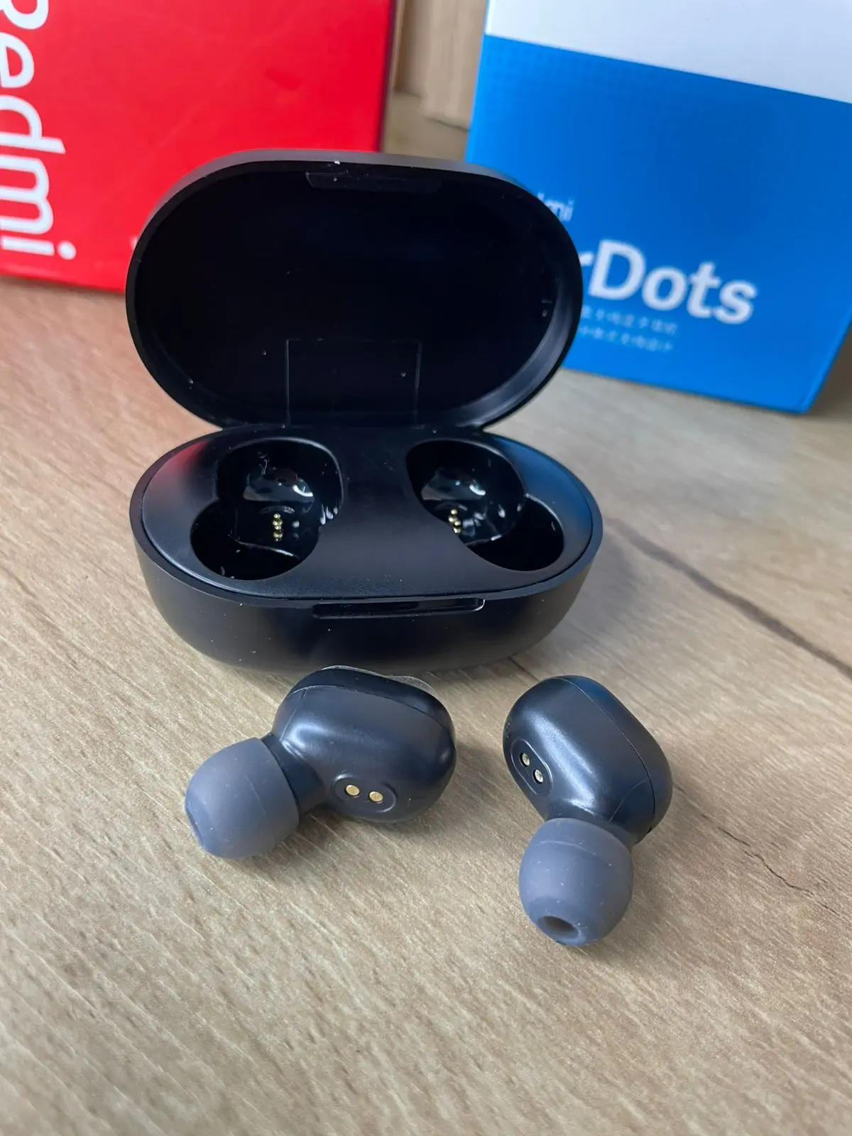 Auriculares inalámbricos Xiaomi Redmi Airdots S negros con puntas de silicona gris y estuche de carga abierto sobre superficie de madera.