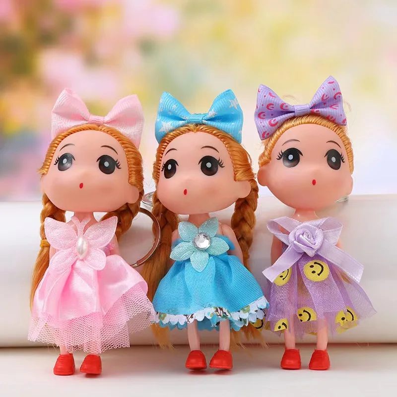 Tres llaveros de muñecas con cabello trenzado, vestidos de tul en colores rosa, azul y morado, con lazos a juego y detalles decorativos en el pecho.