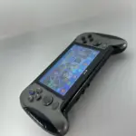 Consola portátil de videojuegos color gris con empuñaduras ergonómicas negras, pantalla táctil encendida y controles físicos en ángulo.