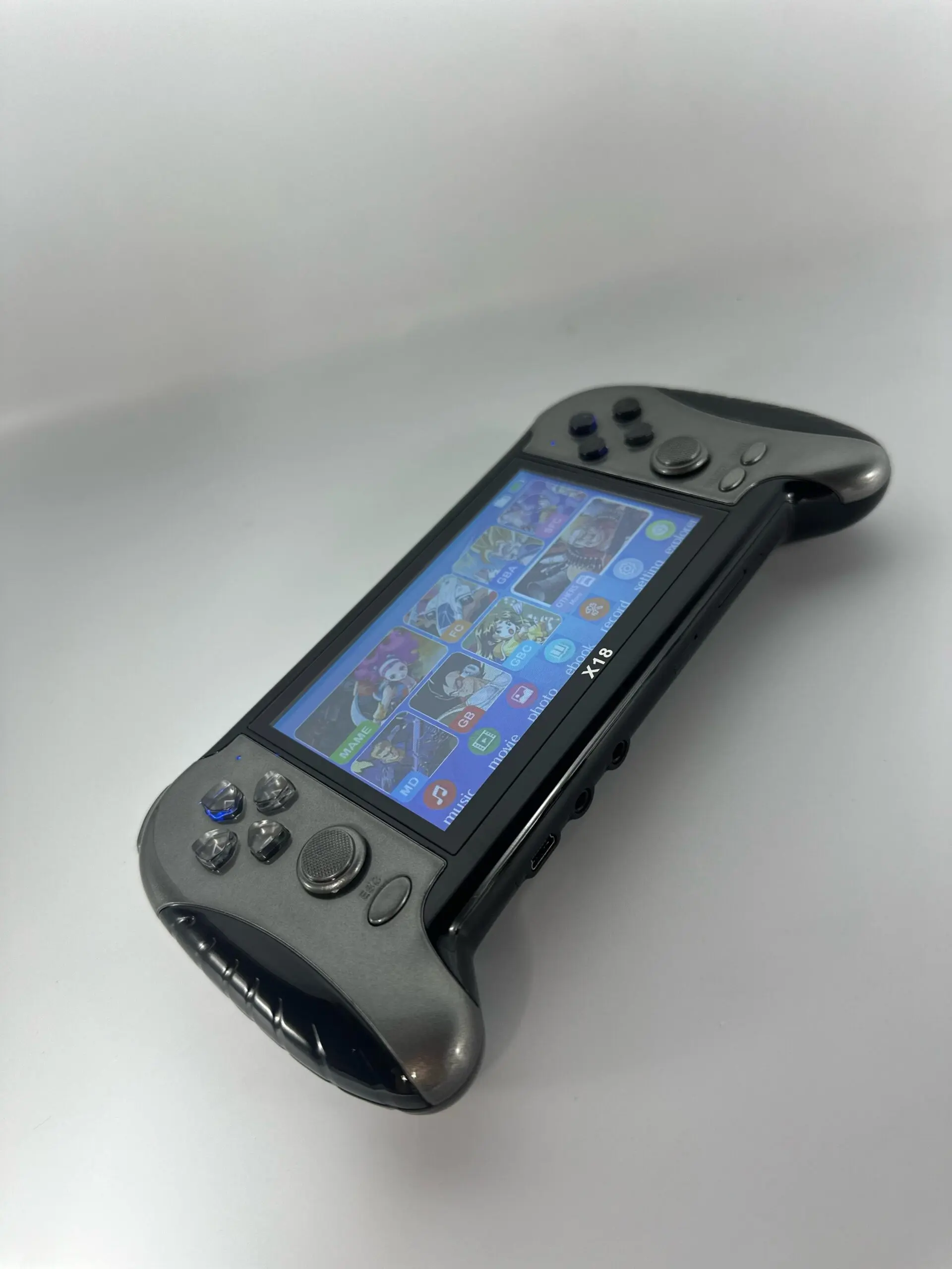Consola portátil de videojuegos color gris con empuñaduras ergonómicas negras, pantalla táctil encendida y controles físicos en ángulo.