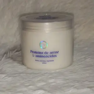 Envase cilíndrico blanco de 300 ml con tapa transparente, etiqueta azul que indica "Proteína de arroz y aminoácidos", sobre fondo texturizado blanco.