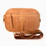 Bolso manos libres de nylon acolchado color caramelo con diseño chevron, bolsillo frontal con cremallera, hebilla decorativa central y correa ajustable.