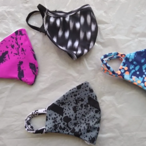 Set de cuatro tapabocas de tela lavables con diseños variados en fucsia, negro, gris y azul con naranja, mostrados extendidos sobre una superficie clara.