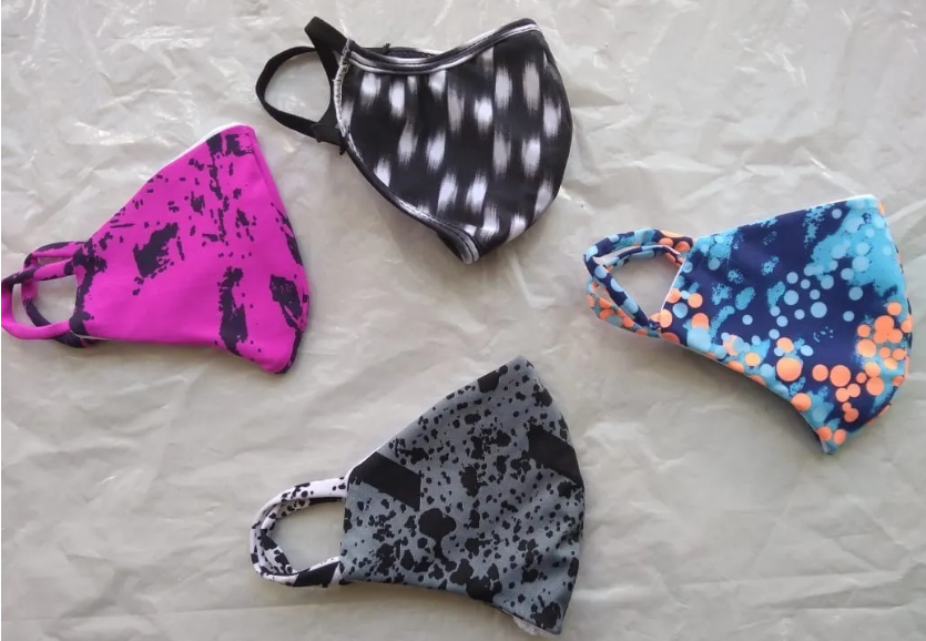 Set de cuatro tapabocas de tela lavables con diseños variados en fucsia, negro, gris y azul con naranja, mostrados extendidos sobre una superficie clara.