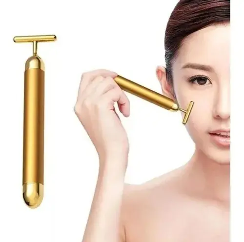 Masajeador facial vibratorio dorado con cabezal en T, mostrado de forma individual y siendo aplicado sobre la mejilla de una mujer.