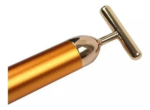 Masajeador facial vibratorio T dorado brillante, cabeza en forma de T y mango metálico cilíndrico, detalle de la punta.