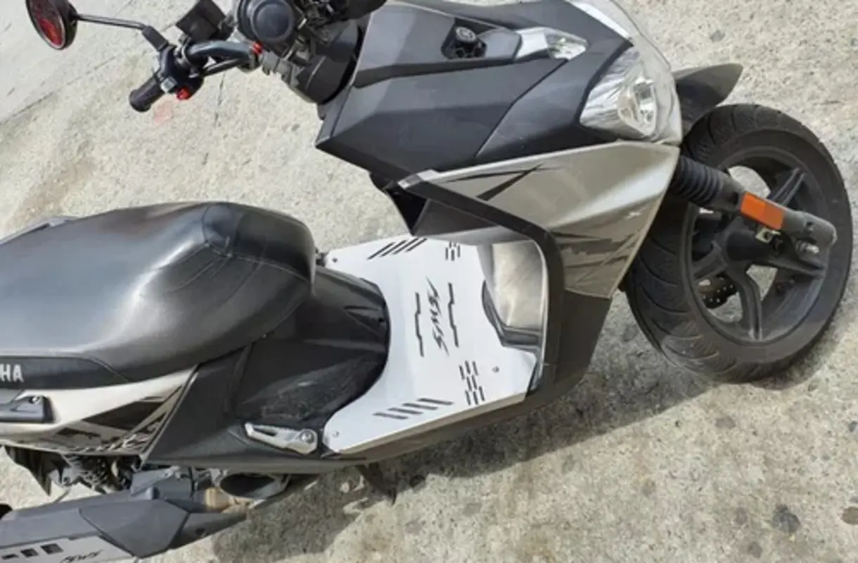Piso protector de acero inoxidable blanco con ranuras antideslizantes instalado en la parte baja de moto BWS gris sobre asfalto.