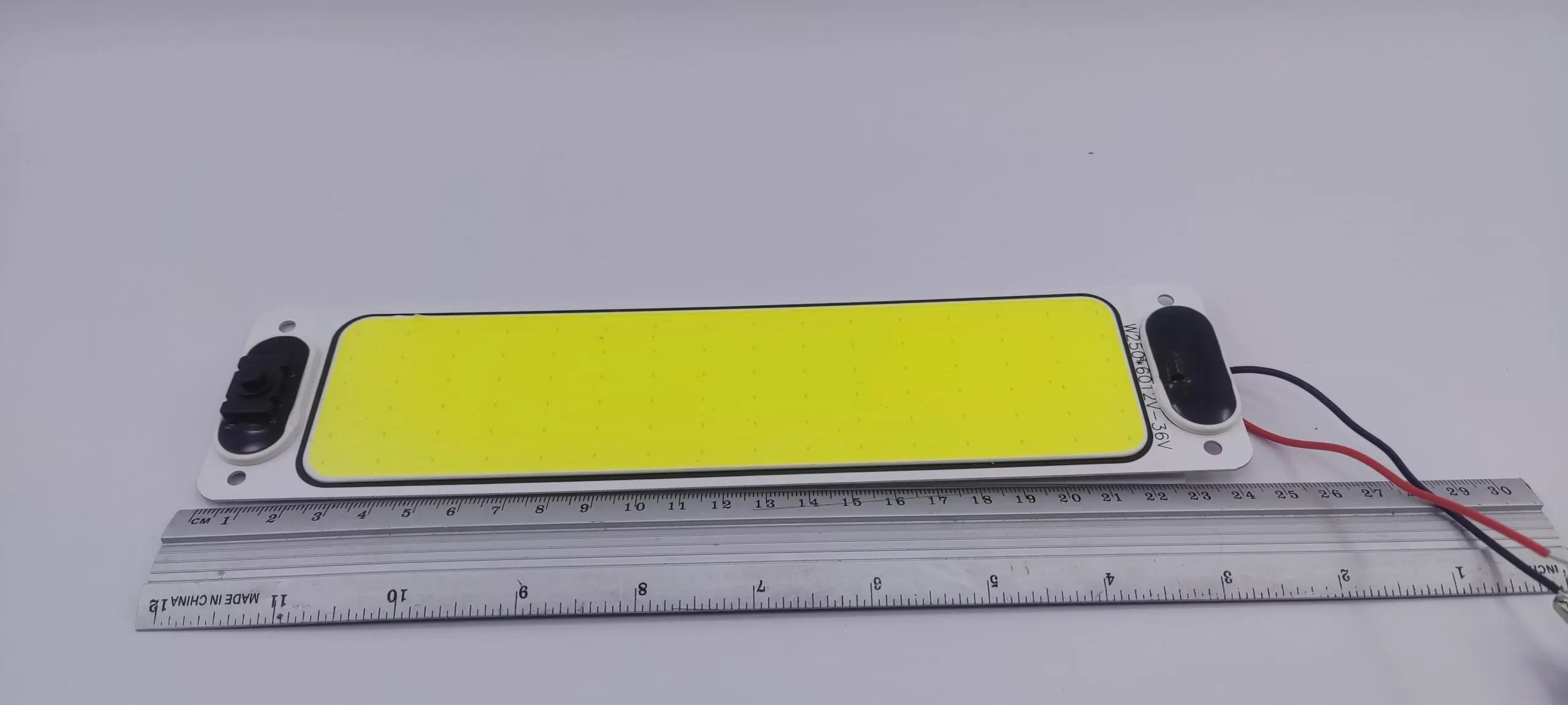 Plaqueta LED rectangular para vehículo con superficie amarilla, marco blanco y cables, junto a una regla que muestra 16 cm de largo.