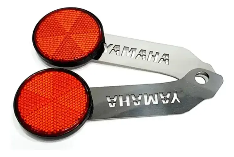 Set de dos tragaluces o reflectores rojos redondos con soportes metálicos plateados de acero inoxidable que llevan troquelada la marca Yamaha, dispuestos en diagonal sobre fondo blanco.