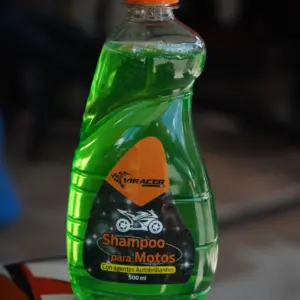 Envase plástico transparente de 500 ml con líquido verde brillante, etiqueta frontal de moto y tapa dosificadora naranja.