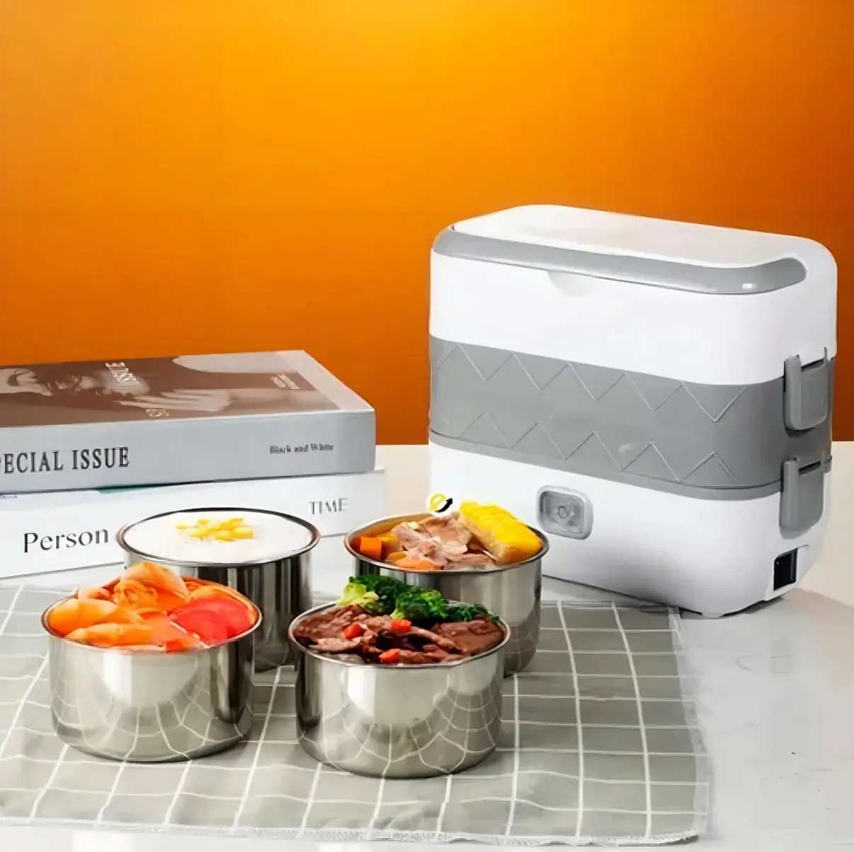 Lonchera eléctrica portátil blanca y gris con cuerpo de doble nivel, cuatro recipientes de acero inoxidable para alimentos y dos libros apilados de fondo.