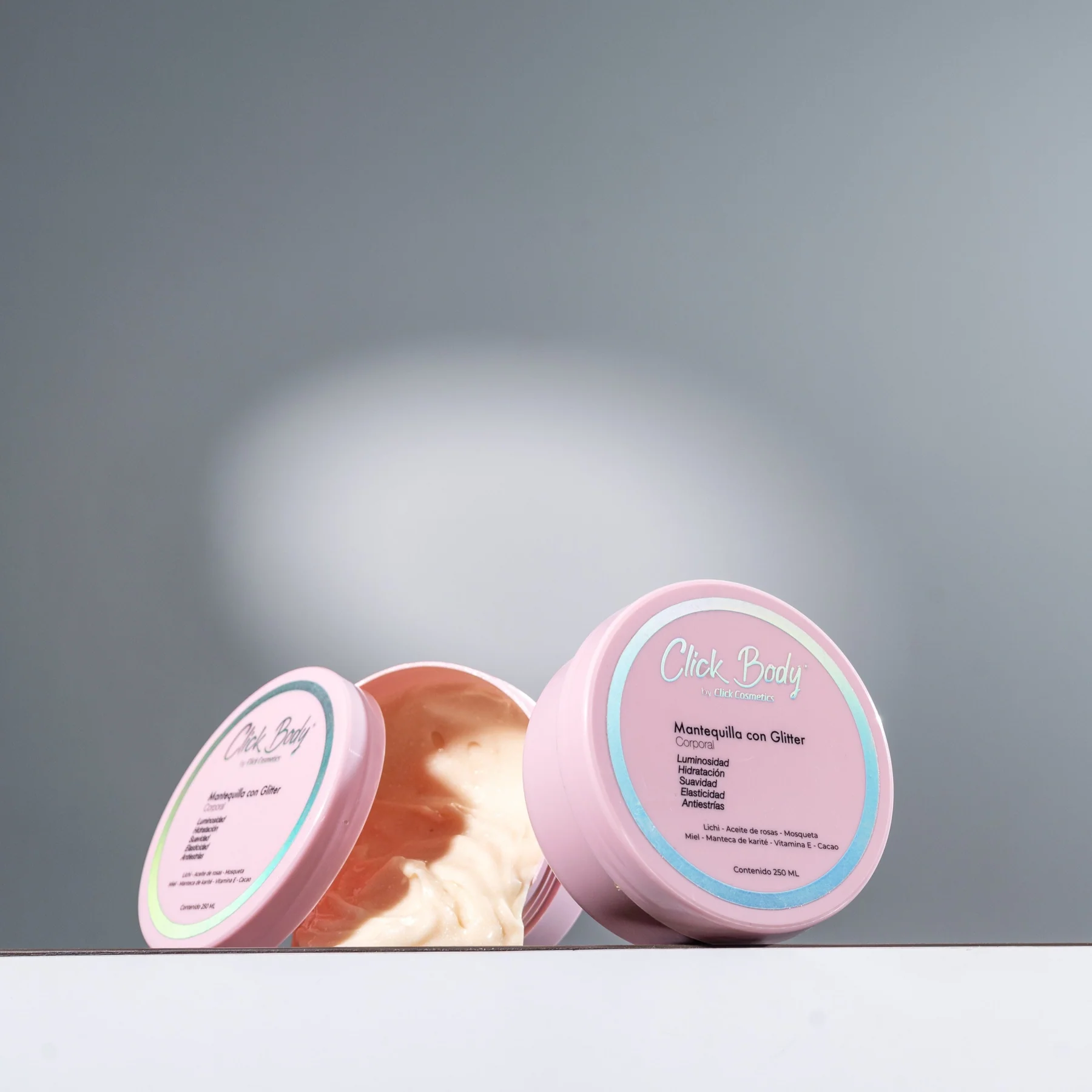 Dos envases rosados de crema corporal con glitter, uno abierto mostrando su textura cremosa y el otro cerrado con etiqueta frontal.