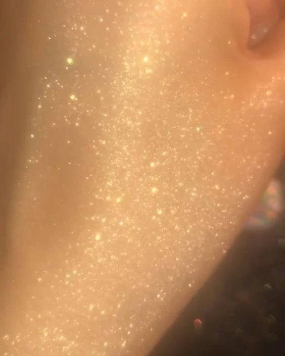 Crema corporal con glitter aplicada en la piel, muestra una textura brillante y luminosa con destellos dorados.