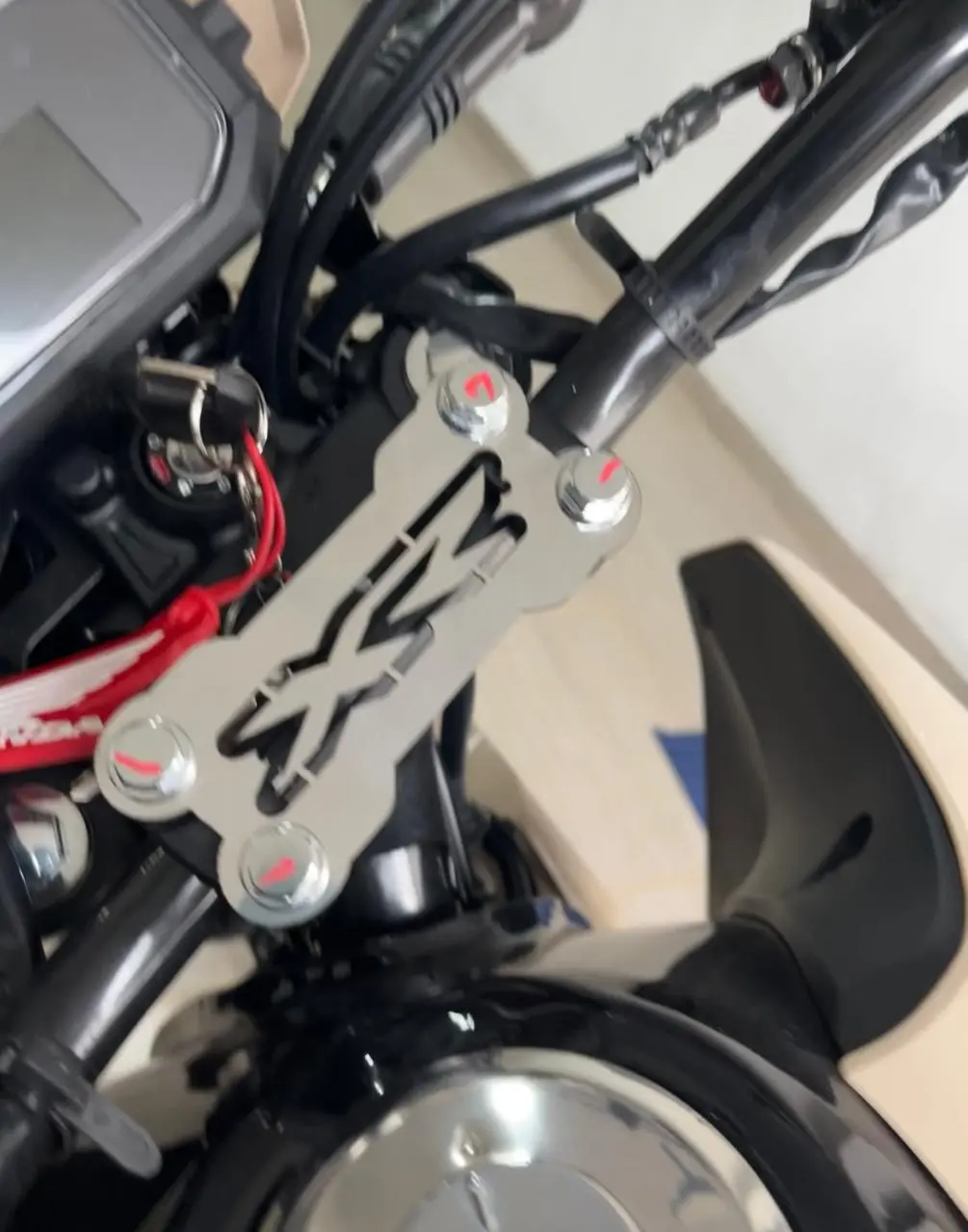 Soporte embellecedor de manubrio plateado en acero inoxidable para moto, diseño perforado con letras estilizadas y cuatro tornillos superiores.