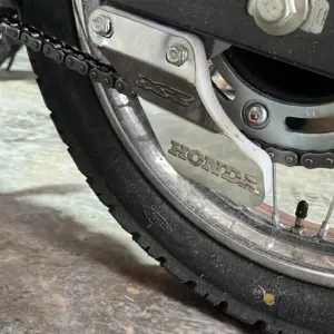 Patín tensor de cadena lateral de acero inoxidable con grabado Honda, instalado en la parte trasera de una motocicleta.