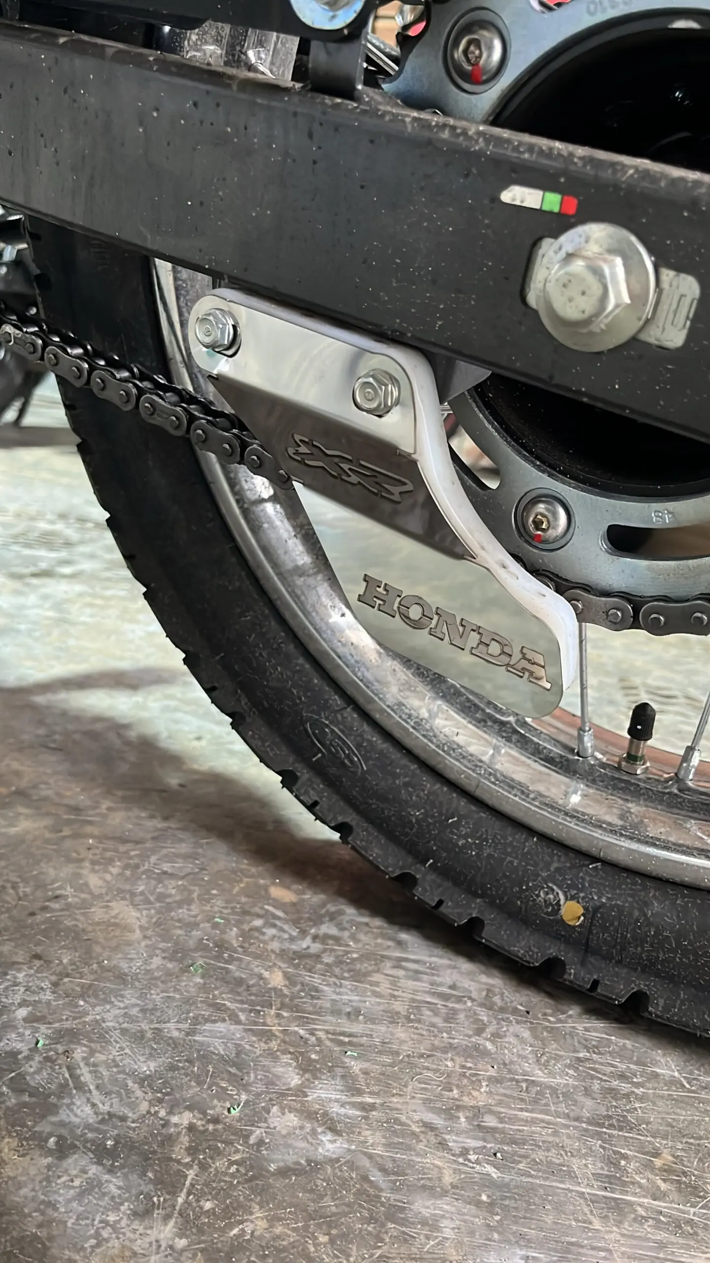 Patín tensor de cadena lateral de acero inoxidable con grabado Honda, instalado en la parte trasera de una motocicleta.