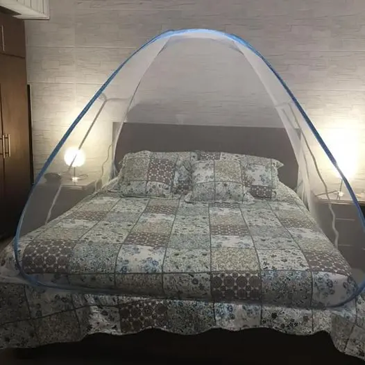 Toldillo portátil con borde azul sobre cama doble con edredón estampado de parches, diseñado para proteger contra insectos y facilitar el descanso.