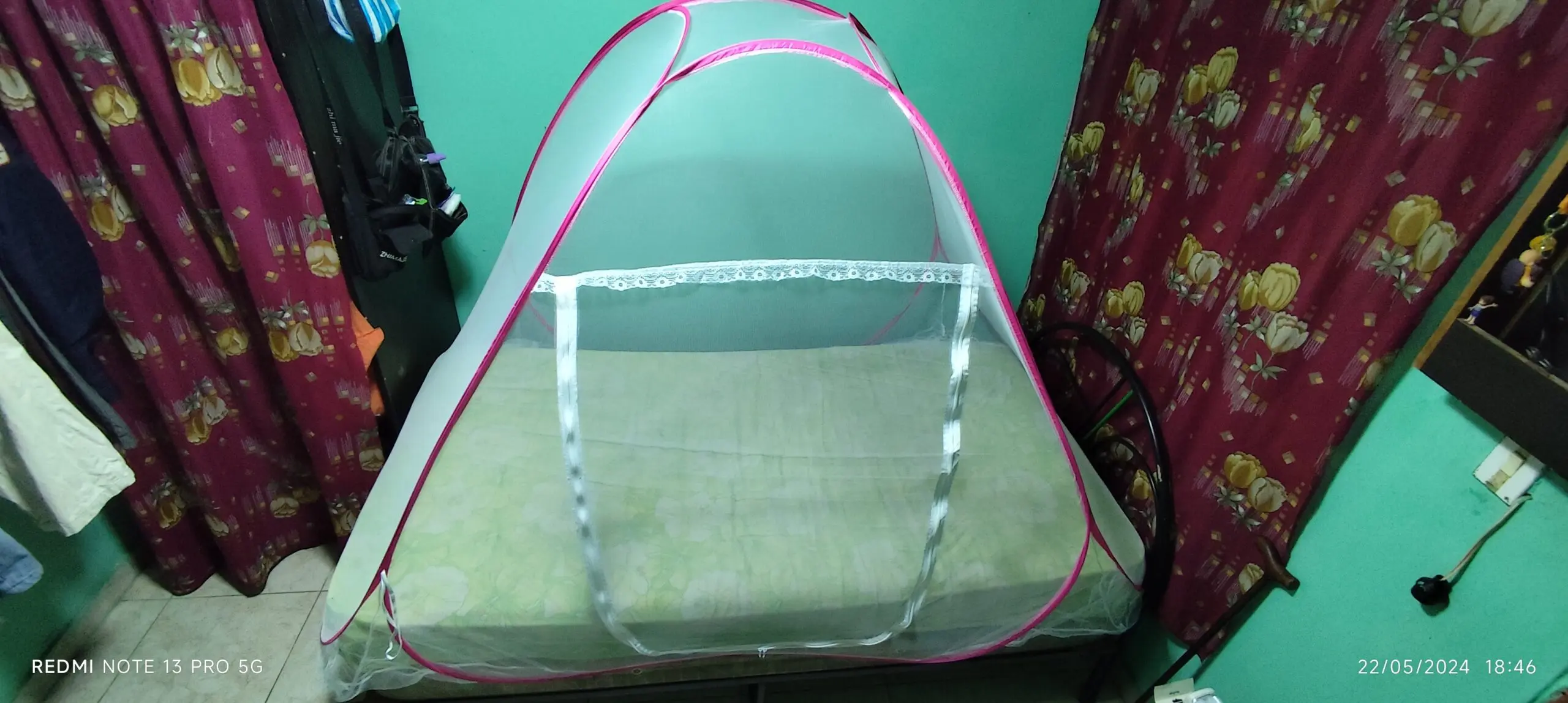 Toldillo portátil para cama con estructura de arcos flexibles, malla blanca traslúcida y bordes en color fucsia, instalado sobre colchón individual.