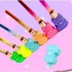 Set de delineadores de ojos waterproof formato violín con punta ergonómica, exhibidos en colores vibrantes sobre fondo rosa con destellos brillantes.