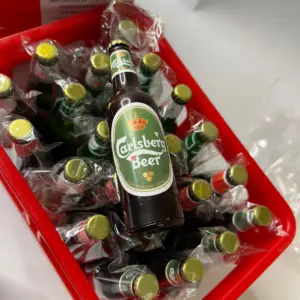 Caja roja organizadora que contiene varios encendedores recargables envueltos individualmente, con la forma y etiqueta de botella de Carlsberg.