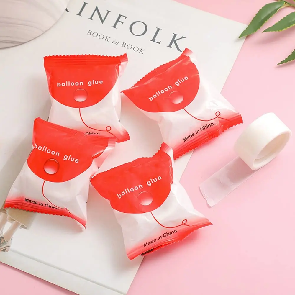 Cuatro sobres rojos de balloon glue y un rollo de adhesivo transparente sobre revista, ideal para manualidades y decoración.