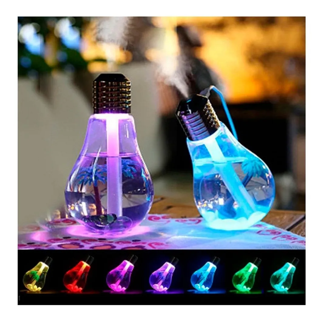 Humidificador difusor de aromas en forma de bombilla con luz LED multicolor, agua, palmeras decorativas y vapor visible sobre mesa de madera.