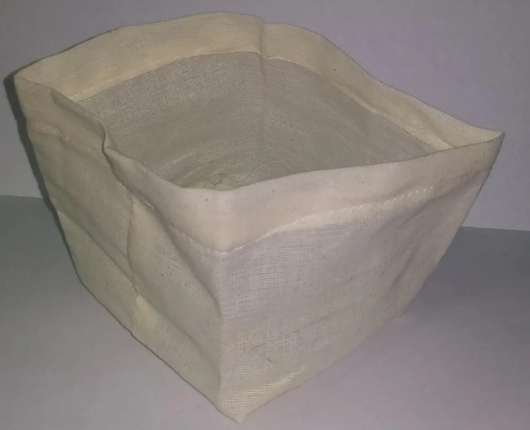 Filtro de tela color crema para greca cafetera, con textura de tejido natural, mostrado en ángulo de tres cuartos sobre fondo blanco.