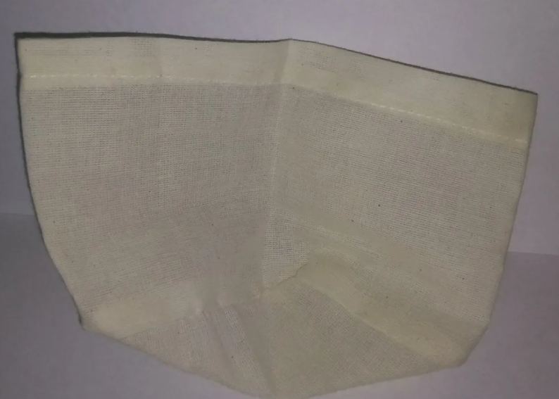 Filtro de tela color crema con textura tejida y forma cónica para greca cafetera, diseñado para retener sedimentos.