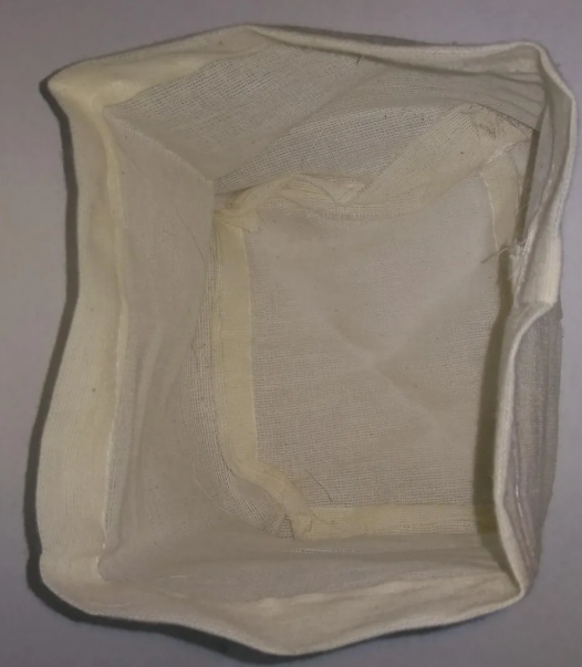 Filtro de tela color crema con textura de tejido resistente y forma rectangular para cafetera de café.
