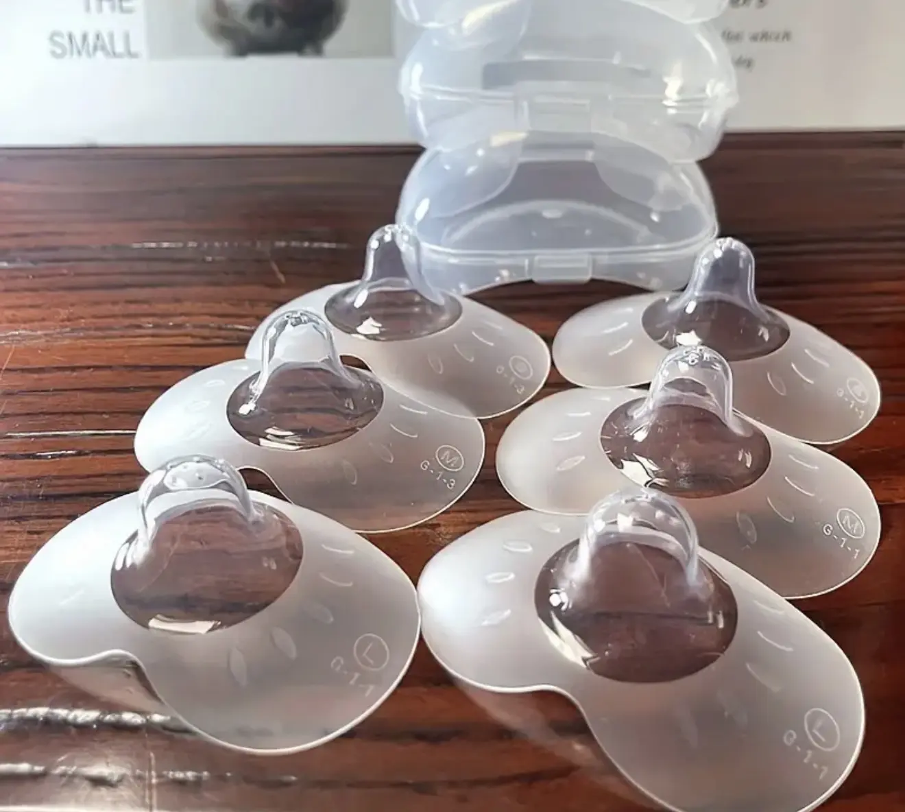 Seis pezoneras de silicona transparente y estuche plástico apilable sobre superficie de madera.