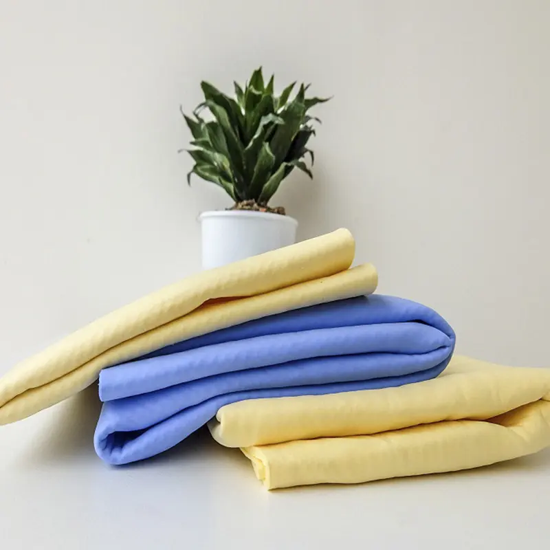 Set de dos toallas de microfibra para cabello, una azul y una amarilla, apiladas sobre una superficie blanca junto a una planta decorativa.