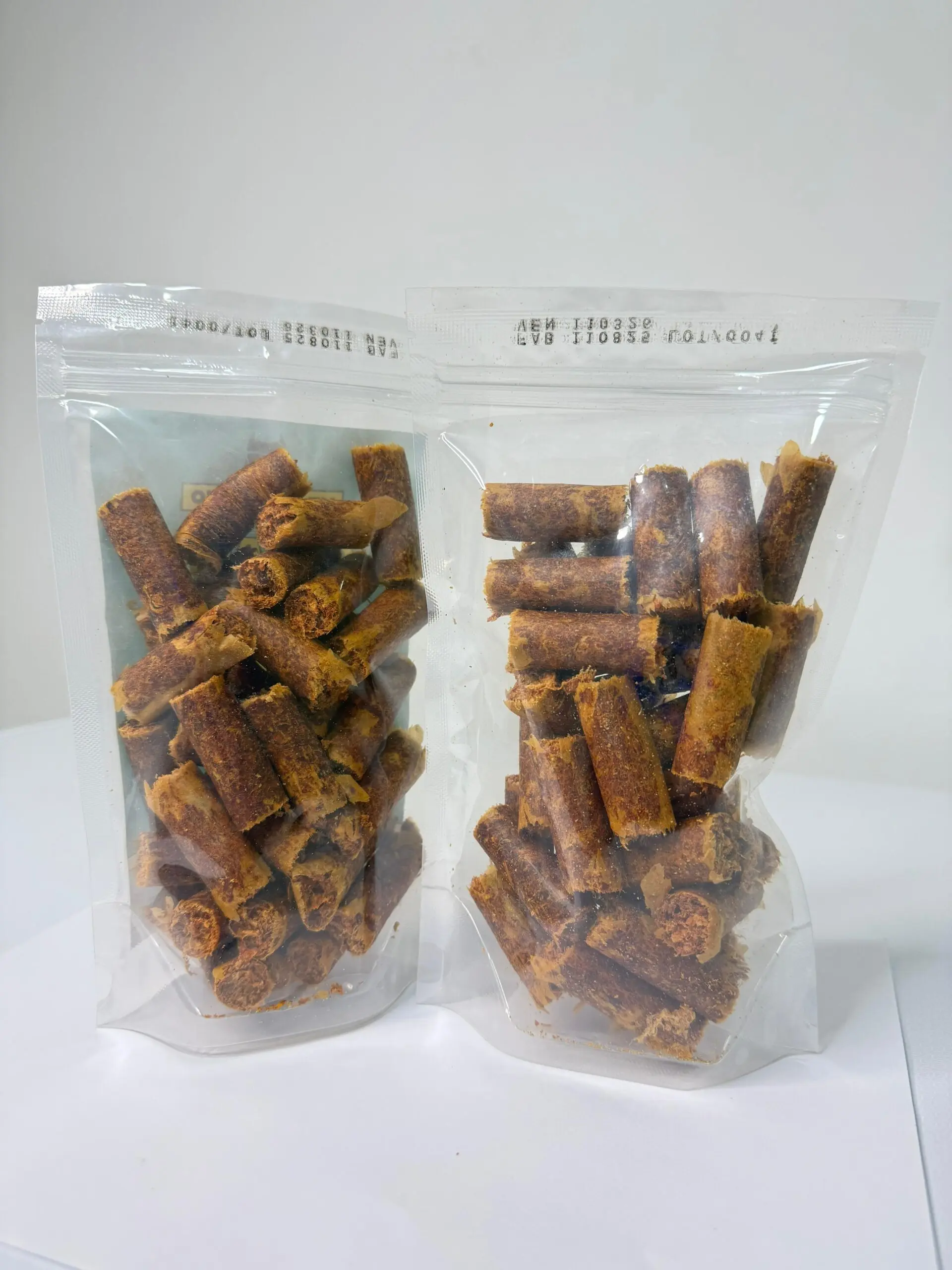 Dos bolsas transparentes con cierre hermético que contienen cabanos de pollo cilíndricos de color marrón para perros y gatos.