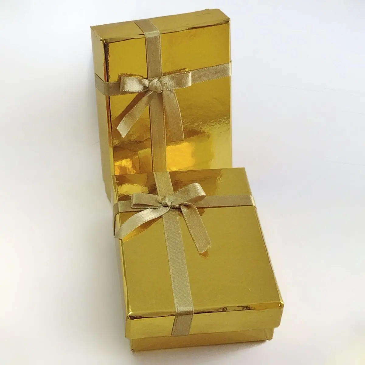 Dos cajas de regalo doradas con lazos de satín y moños sobre fondo blanco, presentación del brazalete Bismark de oro 18K.