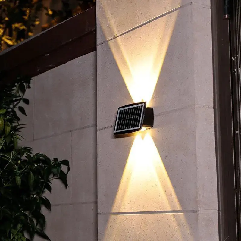 Lámpara solar LED de pared negra con diseño de doble haz de luz arriba y abajo, instalada sobre muro exterior texturizado.