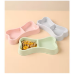 Tres comederos dobles con forma de hueso en colores rosa, gris y verde menta. El modelo verde contiene croquetas en un compartimento.