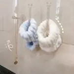 Tres ganchos de pared decorativos con acabado brillante sostienen un collar dorado y dos muñequeras de forro polar suave en colores azul y blanco.