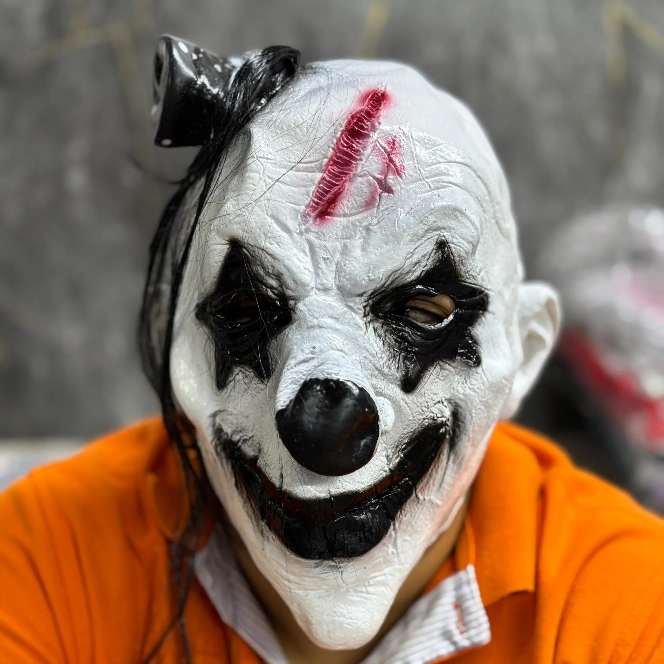 Máscara de látex blanca de payaso aterrador con maquillaje negro en los ojos, nariz redonda, boca sonriente siniestra y herida roja en la frente.