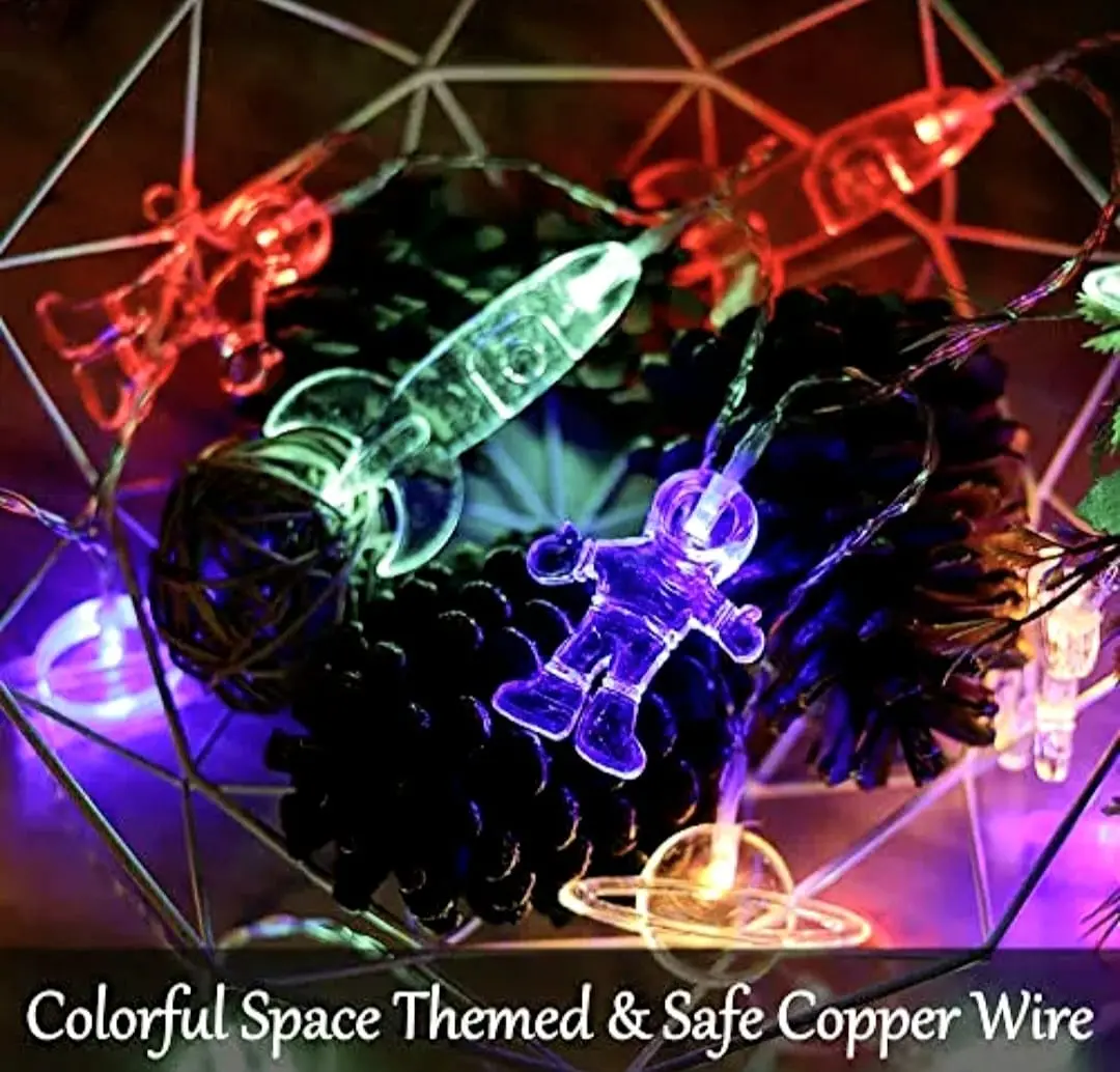Luces LED decorativas espaciales con astronautas y cohetes transparentes iluminados sobre piñas en cesta metálica.