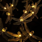 Guirnalda de luces LED con libélulas de alas transparentes texturizadas y luz cálida dorada sobre fondo oscuro.