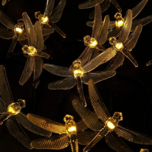 Guirnalda de luces LED con libélulas de alas transparentes texturizadas y luz cálida dorada sobre fondo oscuro.