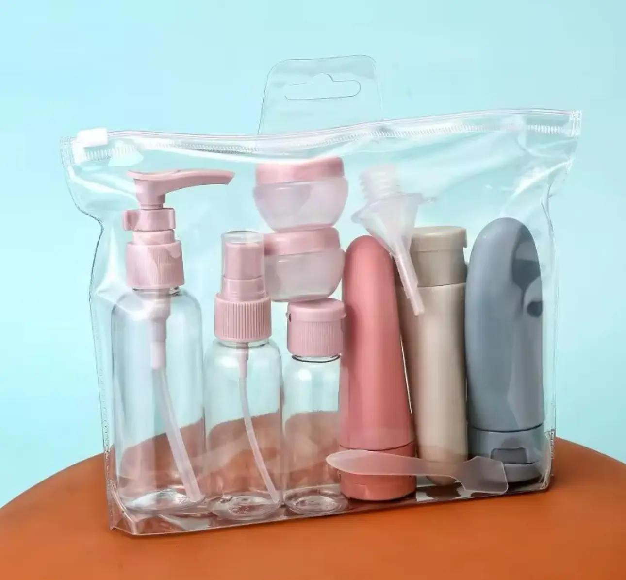 Set de viaje de 11 piezas en estuche transparente con cierre, incluye botellas con bomba, atomizadores, tarros y accesorios en tonos rosa, beige y gris.