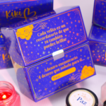 Caja de regalo azul decorada con estrellas doradas y frases motivacionales, acompañada de velas aromáticas.
