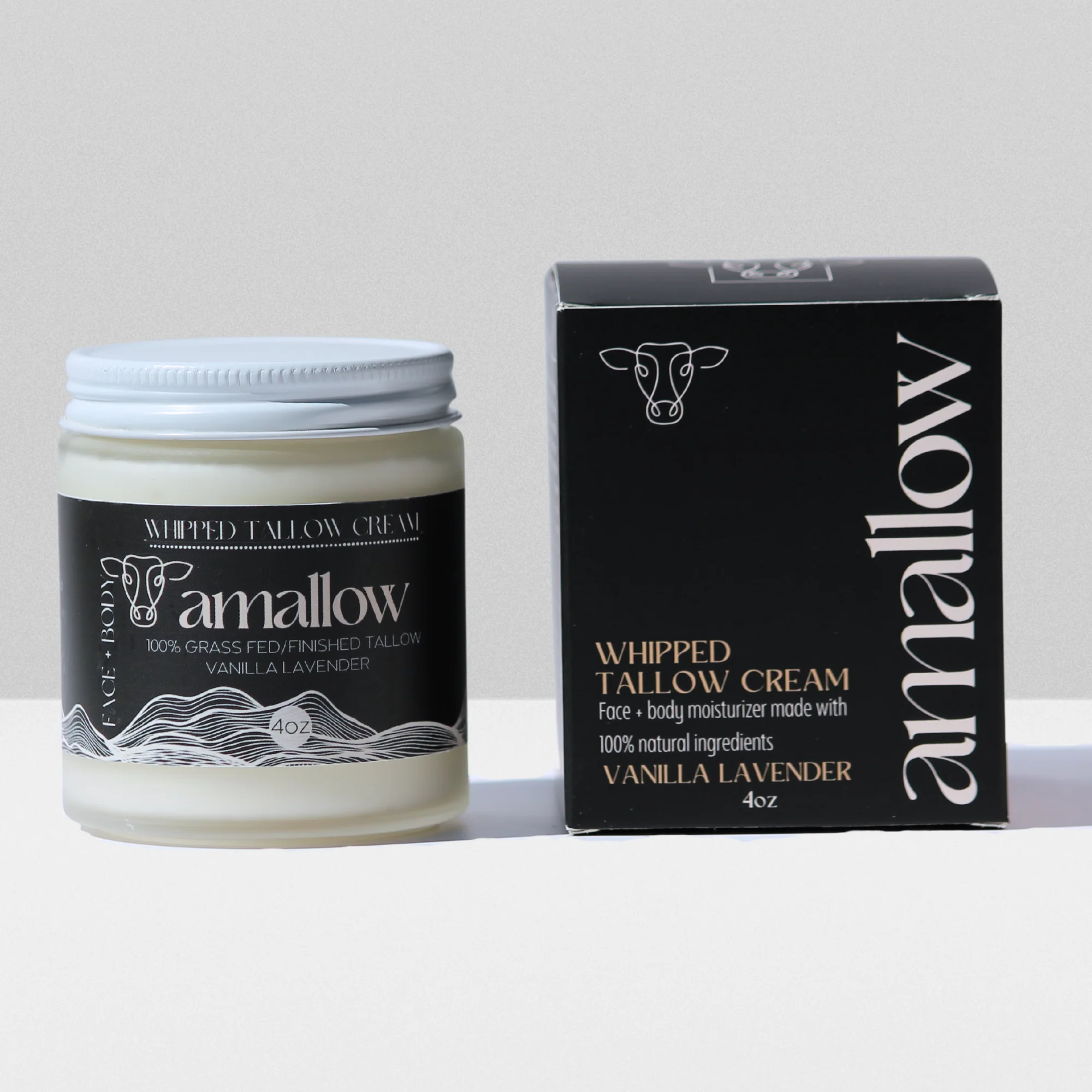 Crema hidratante de sebo batido Amallow aroma vainilla lavanda en frasco de vidrio de 4 oz con tapa blanca junto a su caja negra.