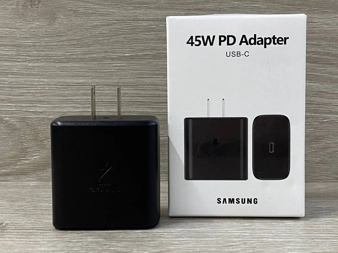 Cargador de pared Samsung USB-C de 45W en color negro con caja de empaque blanca sobre superficie de madera.