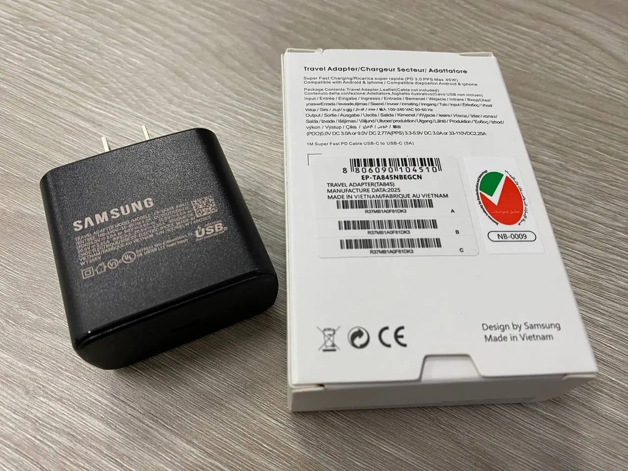 Cargador Samsung de pared negro con puerto USB-C y su caja blanca original sobre superficie de madera clara.
