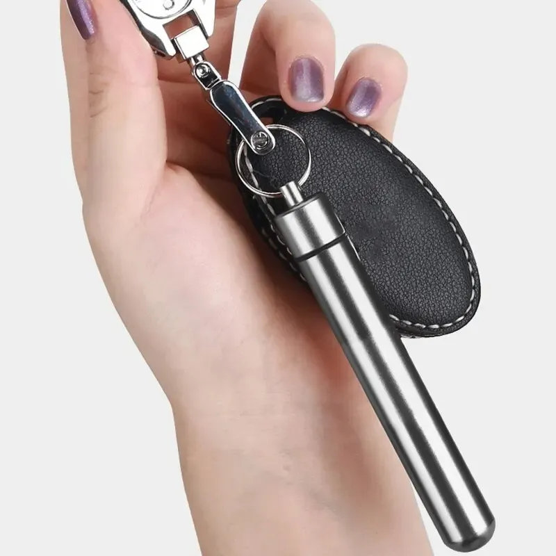 Removedor de cera para oídos de acero inoxidable plateado con estuche negro de cuero sintético, colgado como llavero en una mano.