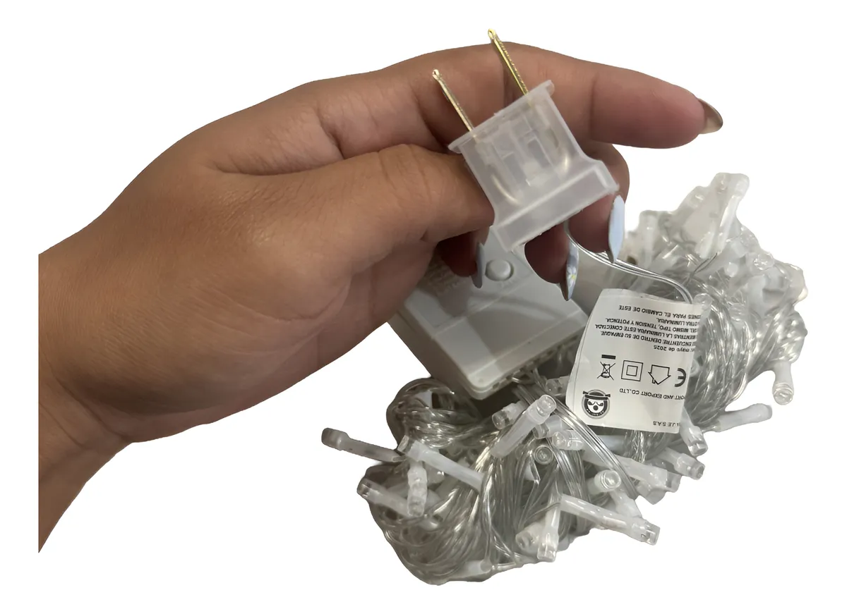 Mano sosteniendo el enchufe de una serie de luces navideñas blancas con caja de control de secuencia y cable transparente enrollado.
