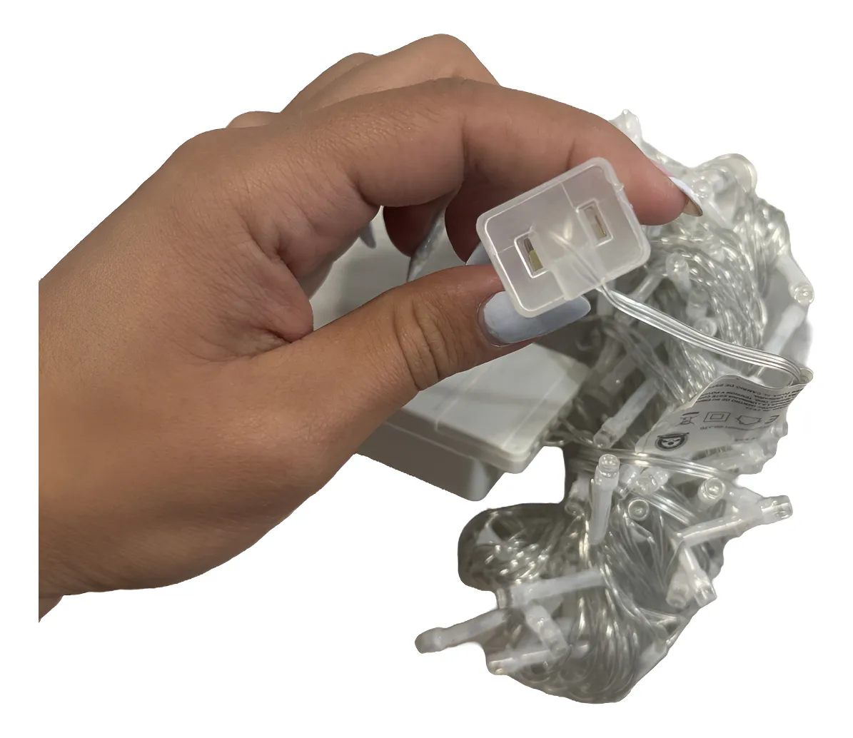 Mano sosteniendo el conector transparente de una serie de luces navideñas de 7 metros con cable blanco y caja de control de secuencias integrada.