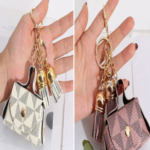 Set x2 llaveros de cuero sintético con monograma y borlas doradas; uno en tono crema y otro en rosa, sostenidos por manos.
